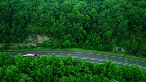 red semi truck with flatbed trailer drives along forest highway past rocky cliff. monteagle
tennessee, usa.