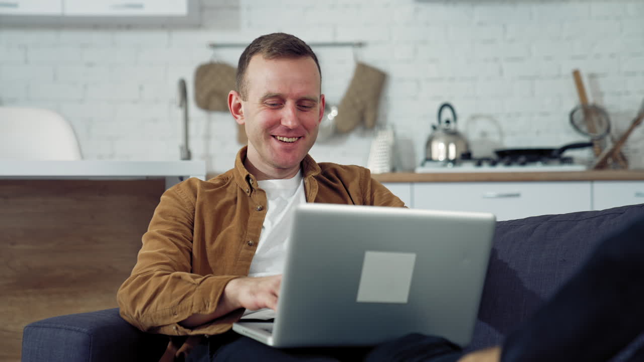 Young man freelancer using laptop in the kitchen. Happy man having a conversation through the laptop. Online working from home. Remote work from home during coronavirus quarantine.