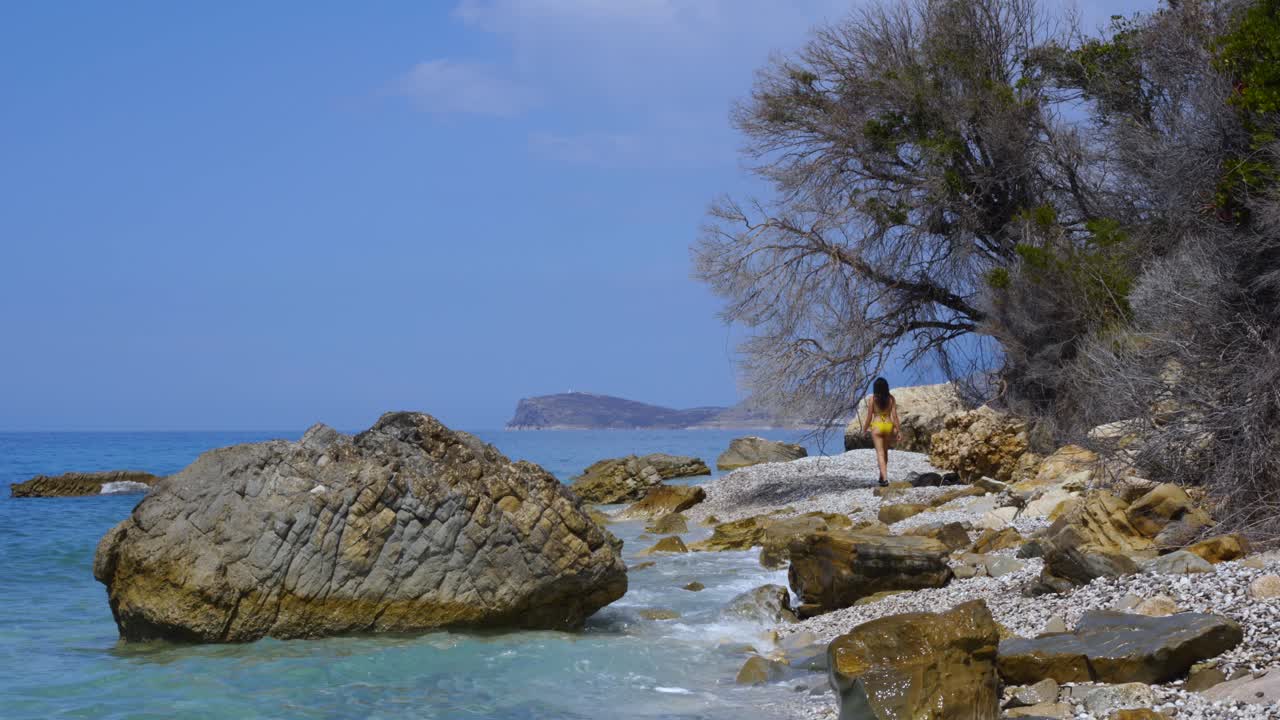 Girl exploring tranquil beach with pebbles and rocks splashed by sea waves in Ionian coastline