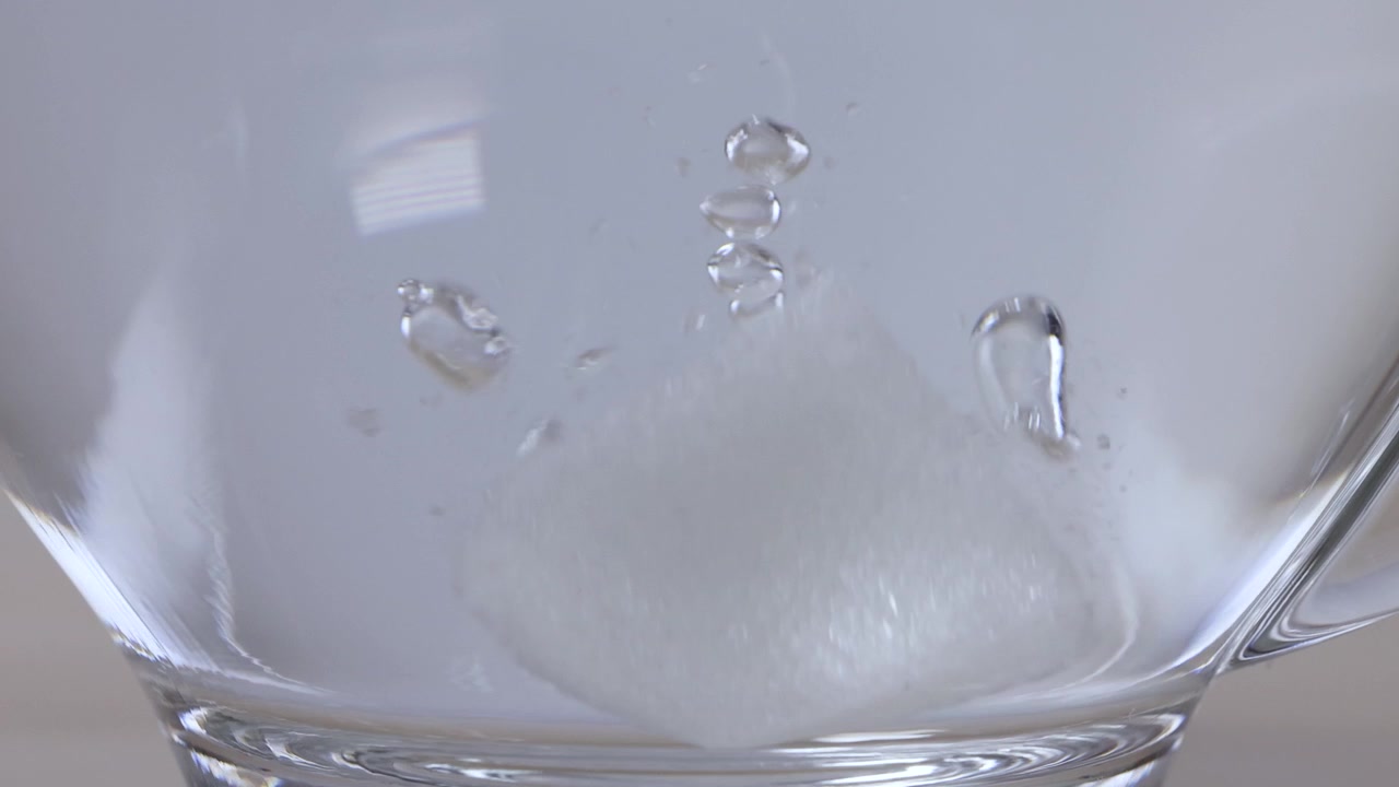 Gros plan sur un morceau de sucre blanc se dissolvant dans de l'eau chaude à l'intérieur d'une tasse en verre transparent