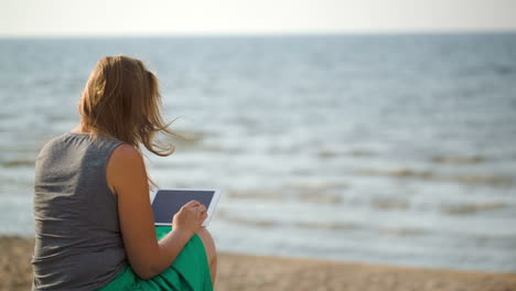 Mujer-Sentada-En-La-Playa-Junto-Al-Mar-Con-Panel-Táctil