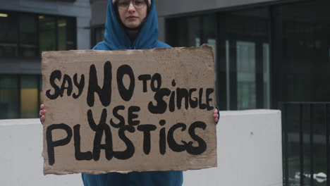 joven activista climática con pancarta protestando contra los plásticos de un solo uso mientras mira la cámara 1