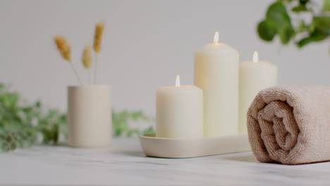 Still-Life-Of-Lit-Candles-With-Dried-Grasses-Green-Plant-And-Soft-Towels-As-Part-Of-Relaxing-Spa-Day-Decor