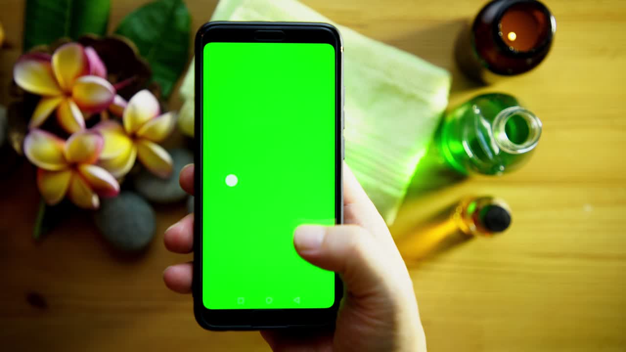 hombre con pantalla verde teléfono inteligente contra frangipani, toalla y aceite de masaje en fondo de madera