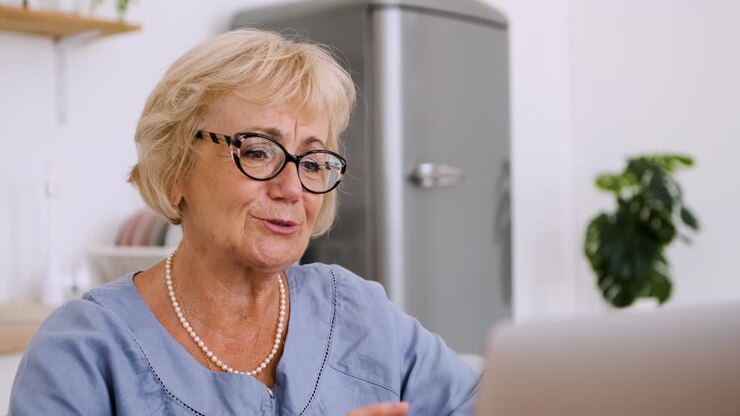Ritratto di una donna anziana felice seduta al tavolo in cucina che parla in videochiamata su un laptop moderno.