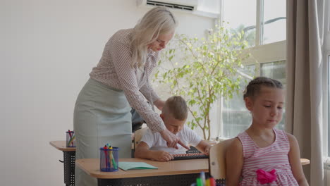 In-Elementary-School-Class:-Enthusiastic-Teacher-walks-between-Rows-of-Bright-Diverse-Children-Explains-Lesson.-Group-of-Smart-Multiethnic-Kids-Learning-New-Stuff.-Side-View-Tracking-Shot