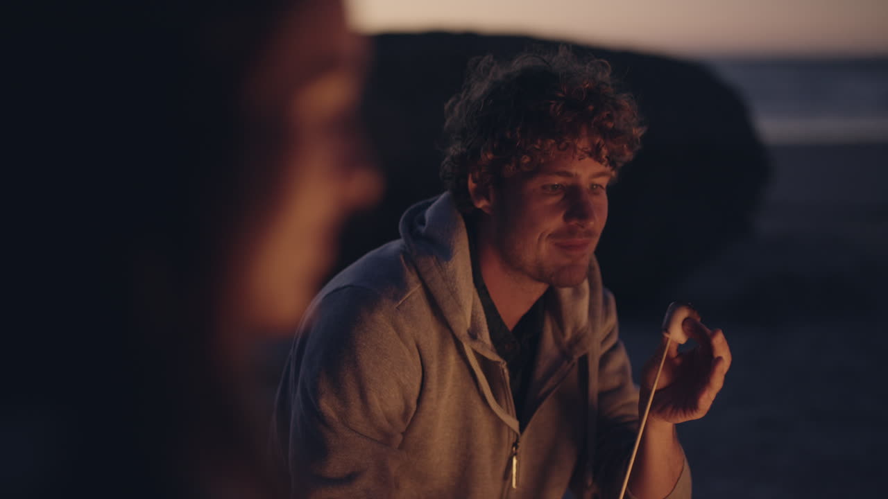 fiesta en la playa al atardecer con hoguera y malvaviscos asados con amigos