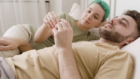 feliz pareja joven tomados de la mano y hablando juntos mientras están acostados en la cama