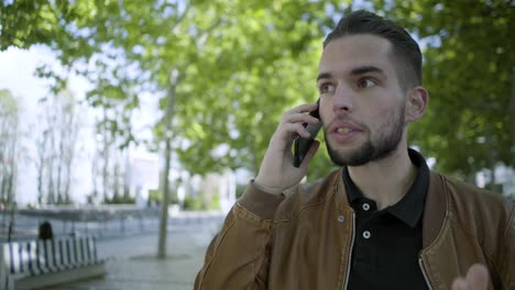 excited young man talking on smartphone while walking in park.