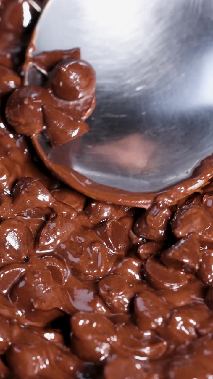 Primo piano di un cucchiaio che mescola delicatamente gocce di cioccolato fuso.