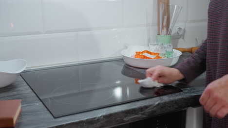 vista lateral de una mujer limpiando una estufa de vidrio elegante en una cocina moderna, con la mano sosteniendo una tela que pulida cuidadosamente la superficie, asegurando la limpieza, la encimera elegante y la decoración minimalista