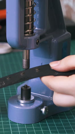 cu: experienced woman worker fixes silver eyelet parts on black leather belt against workshop equipment closeup