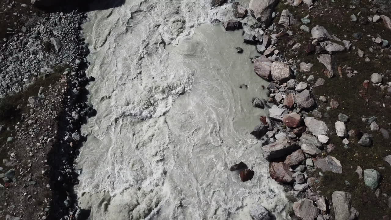 вид сверху с беспилотника на коричневую грязную горную реку с пеной, образовавшейся из-за сильного течения, долина швейцарских альп