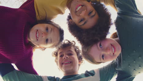 retrato de bajo ángulo de niños divirtiéndose jugando al aire libre uniendo brazos mirando hacia abajo en la cámara