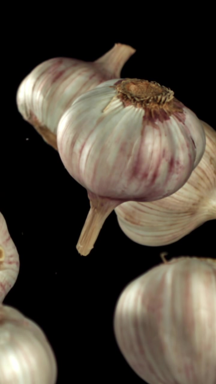 Teste d'aglio fresche che galleggiano al rallentatore su sfondo nero