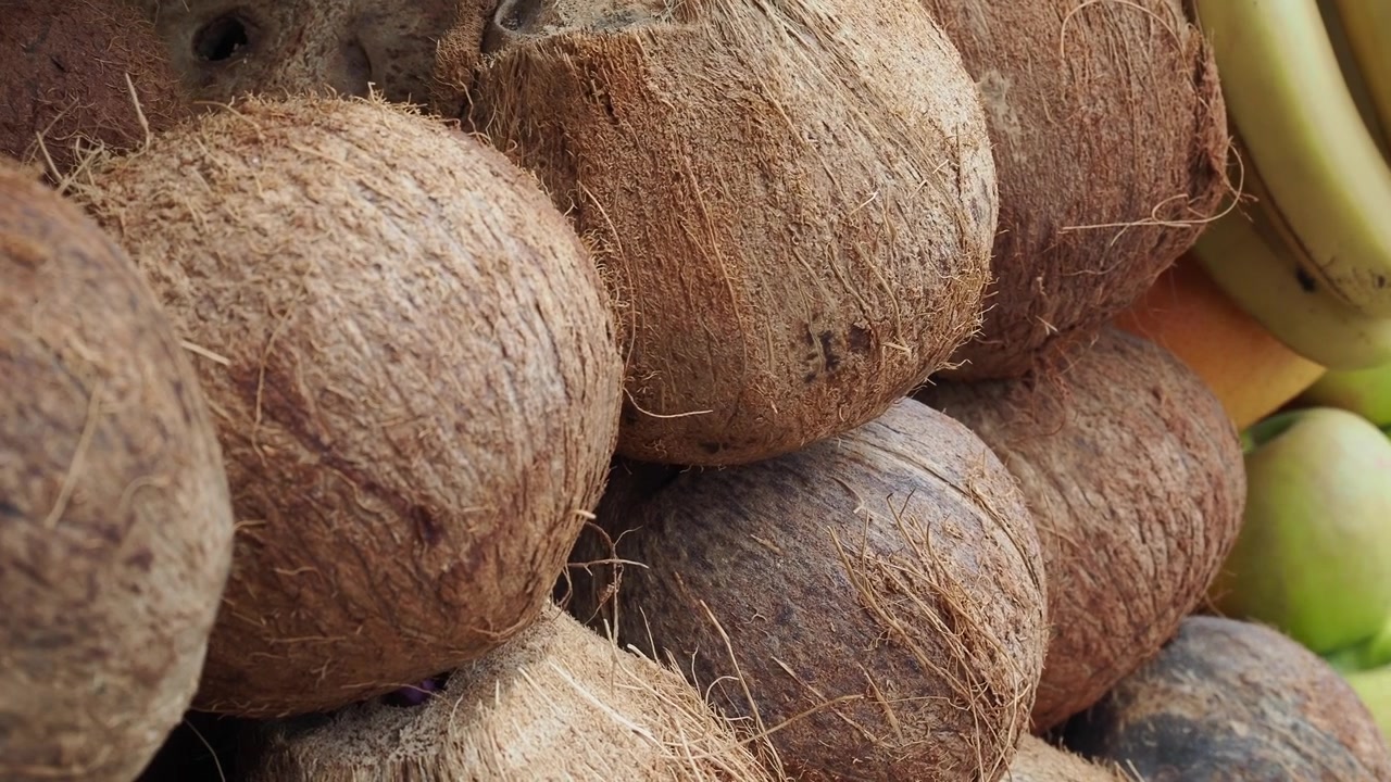 Stack of Fresh Coconuts and Assorted Fruit at a Market