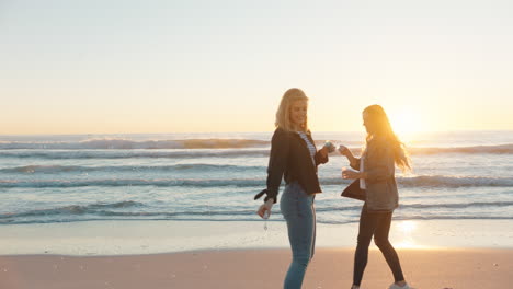 Freundinnen-Blasen-Am-Strand-Bei-Sonnenuntergang-Seifenblasen-Und-Haben-Spaß-Im-Sommer,-Spielen-Am-Meer-Und-Genießen-Die-Freundschaft