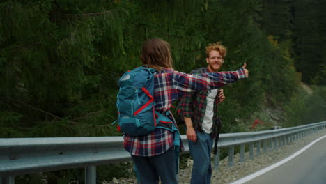 travelers hitchhiking car together in mountains. couple show thumbs up on road.