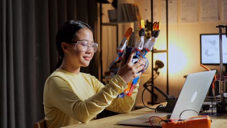 teen asian girl with a laptop checking a cyborg hand at home