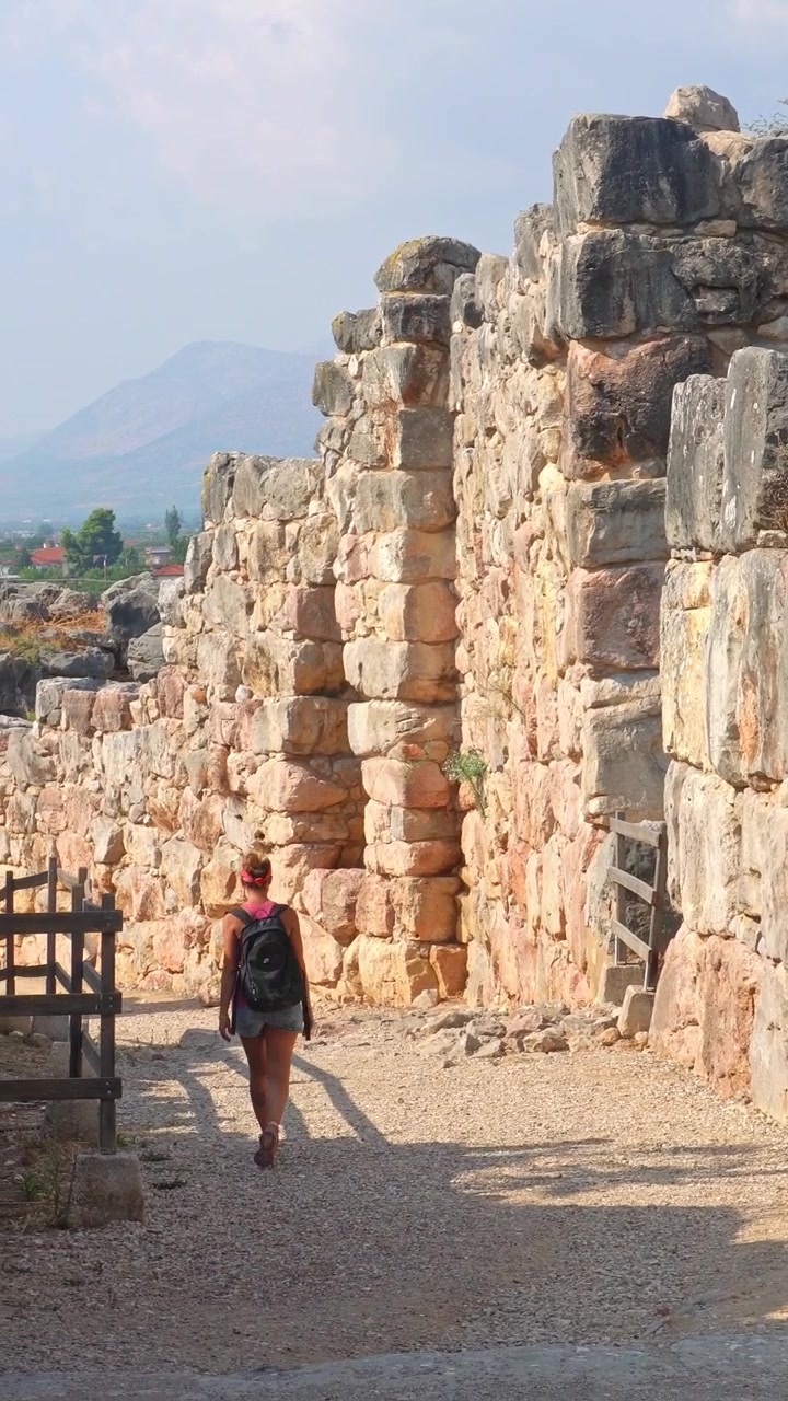 Giovane donna che cammina tra le antiche rovine della cittadella di Tirinto in Grecia