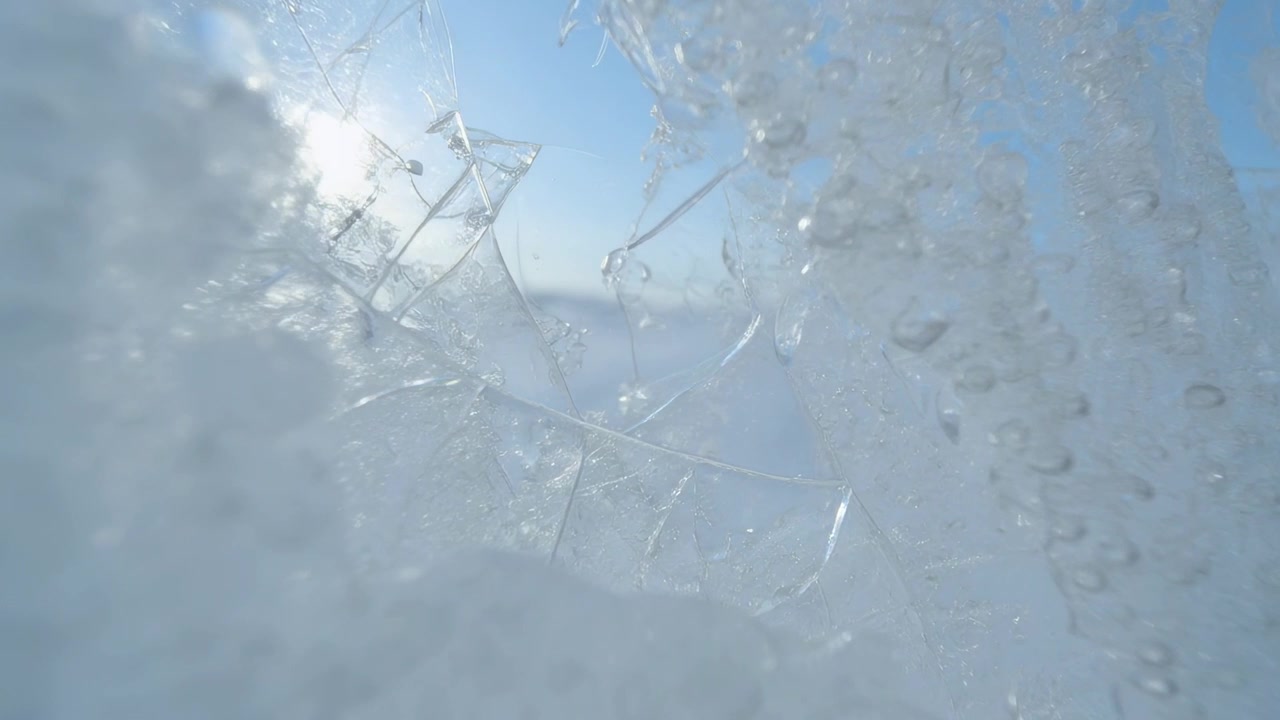 Melting translucent ice formation revealing blue sky outdoors, bright sun causing droplets to merge
