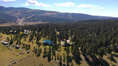 Aerial-Angel-Fire,-New-Mexico-flight-over-wooded-town-with-Ski-Resort-in-background-Summer