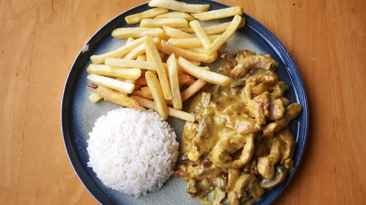 persona comiendo un plato de pollo, arroz y papas fritas