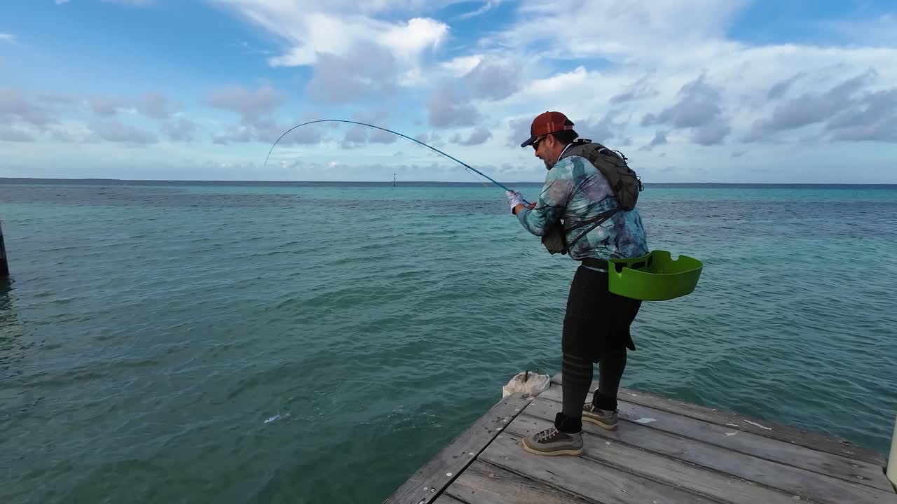 hombre de pesca deportiva pez hueso con caña de pesca en un muelle de madera, mar del caribe los rocas