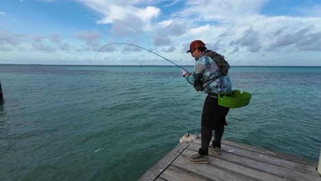 man sport fishing bonefish with fishing rod on wooden dock, caribbean sea los roques