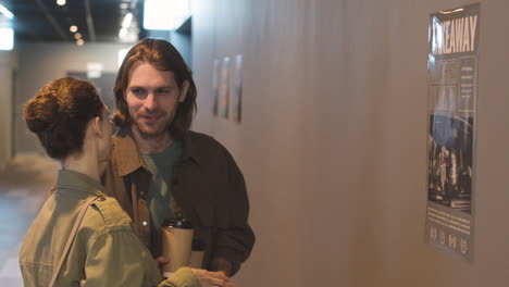 happy couple with a takeaway drink talking together while looking a wall poster at the cinema 1