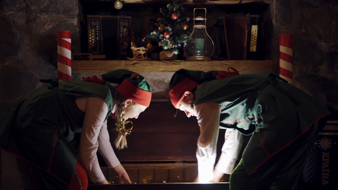 Surprised elves open the big chest in darkness. Santa's helpers elves open magic chest and taking beautiful box on Christmas decor background.