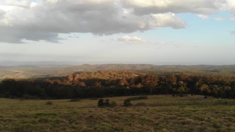 Drone-flight-over-the-Australian-outback-landscape-at-sunset,-with-trees-and-clouds