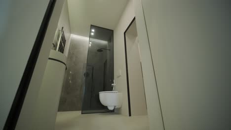 a sleek and modern bathroom featuring a glass-enclosed shower, wall-mounted toilet, and elegant marble tiles. the space is designed with a minimalist aesthetic, emphasizing clean lines and functionality.