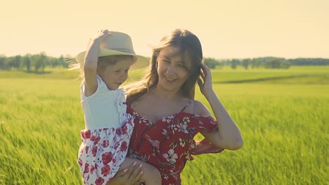 cu slow motion mom with little daughter in her arms walking along field they are dressed in summer dresses