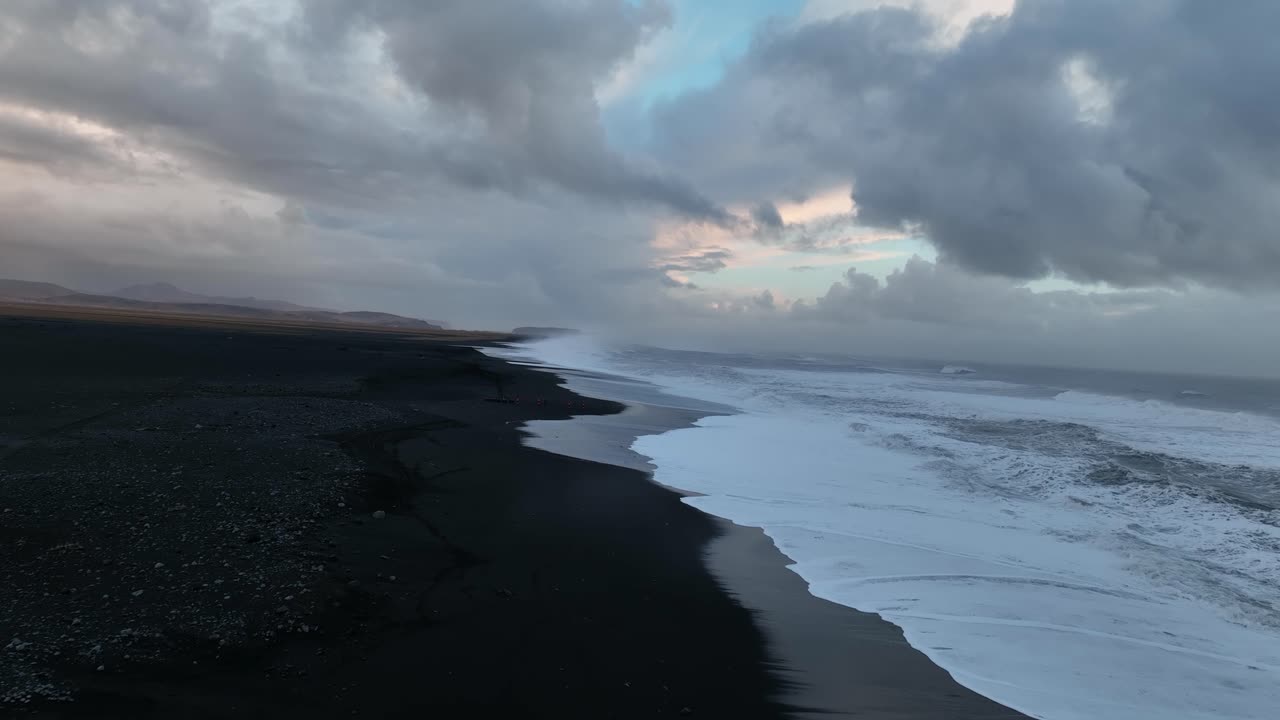 Aerial landscape view of ocean waves crashing on Iceland S&oacute;lheimasandur black sand beach, during a cloudy sunset
