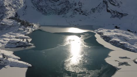 aerial flight forward over freezing lake trübsee near engelberg in switzerland with lots of fresh snow on the shores and an alpine backdrop