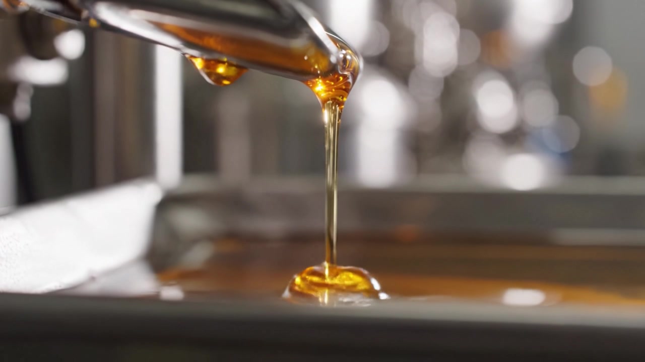 Primo piano di liquido che scorre da un tubo, catturando il colore ricco e ambrato e la texture lucida della sostanza in un ambiente di produzione.