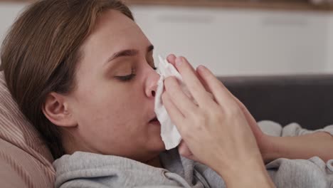 close up of sick caucasian woman lying down and wipes nose.