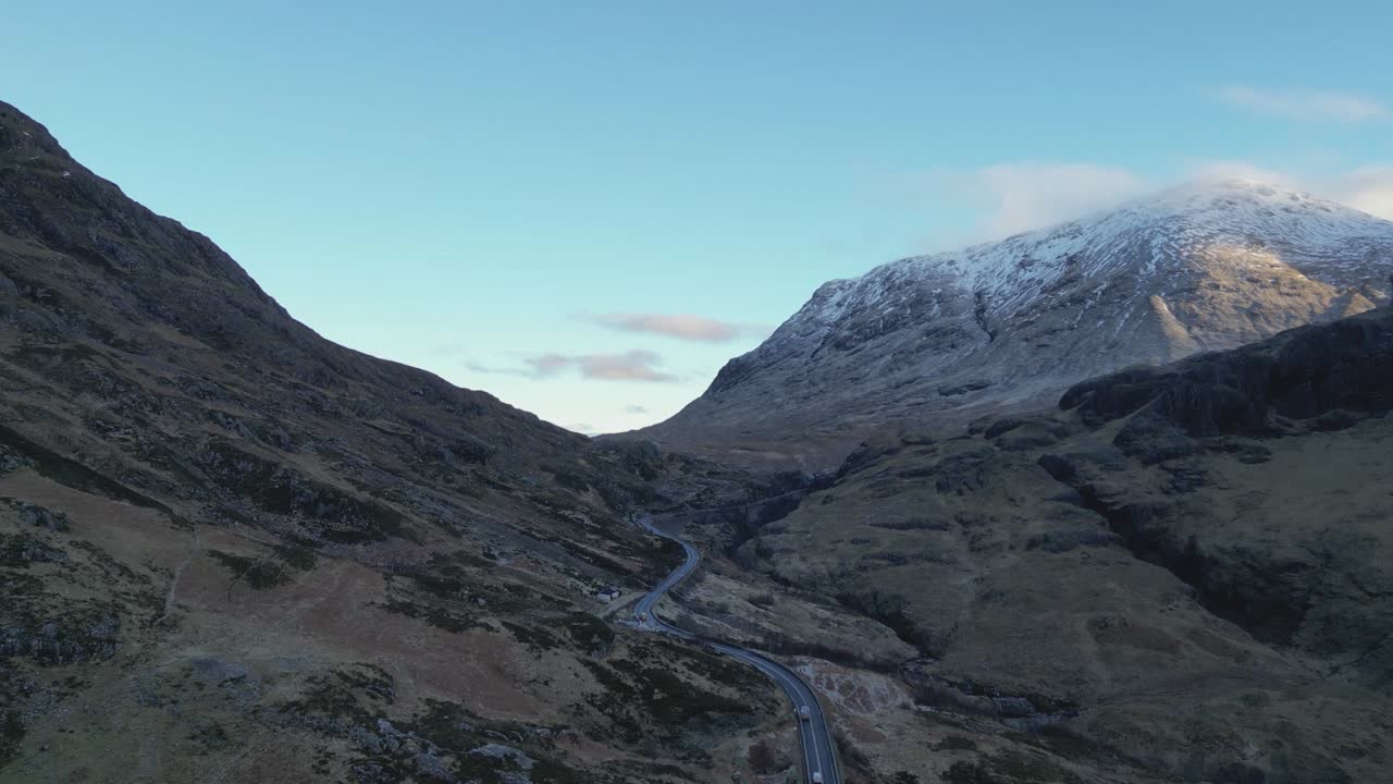 Carretera sinuosa a través de las montañas nevadas de Glencoe al anochecer, serena y majestuosa, vista aérea.