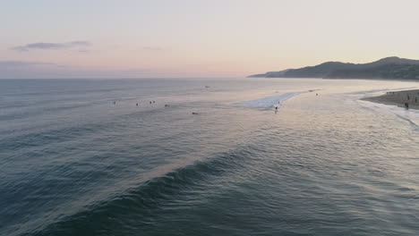 Verfolgung-Der-Antenne,-Die-Der-Welle-Folgt,-Während-Surfer-Bei-Sonnenaufgang-Zum-Ufer-Fahren,-4k