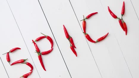 a word spicy formed with small red chilli peppers  placed on white wooden table