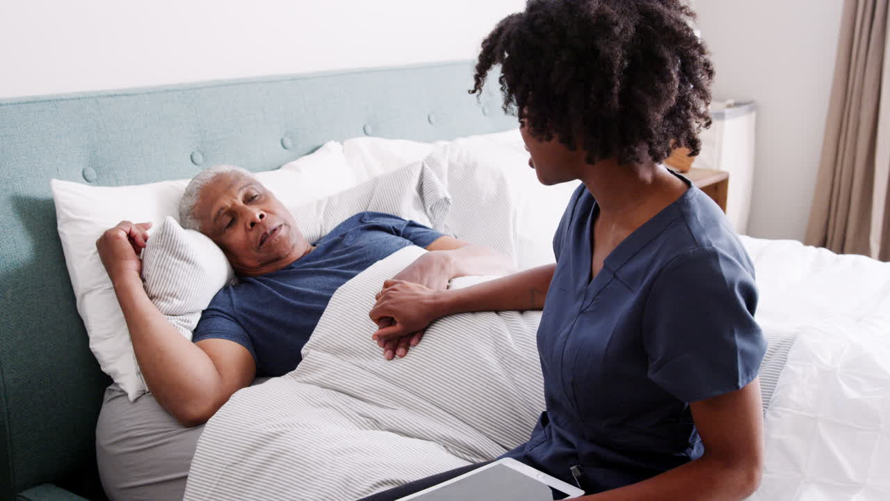 Nurse Visiting Senior Man Lying In Bed Suffering With Illness