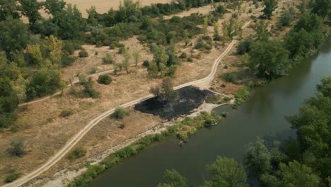 Luftaufnahme-Von-Verbranntem-Trockenem-Gras-Am-Fluss-Im-Sonnigen-Sommer,-Europa