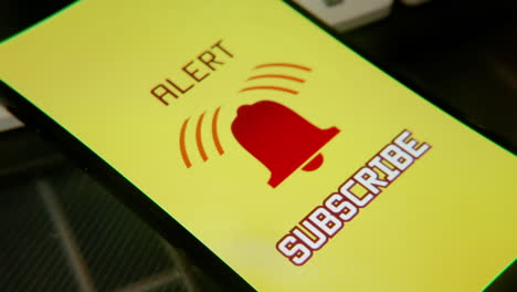 a ringing bell alarm appearing on a smartphone, with a red shaking icon and the texts alert, subscribe