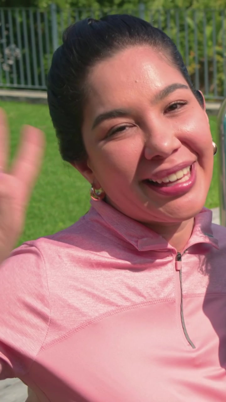 Video verticale: Telefono che suona, donna che fa il segno della pace, sorride al parco con un top rosa e orecchini a cerchio d'oro.