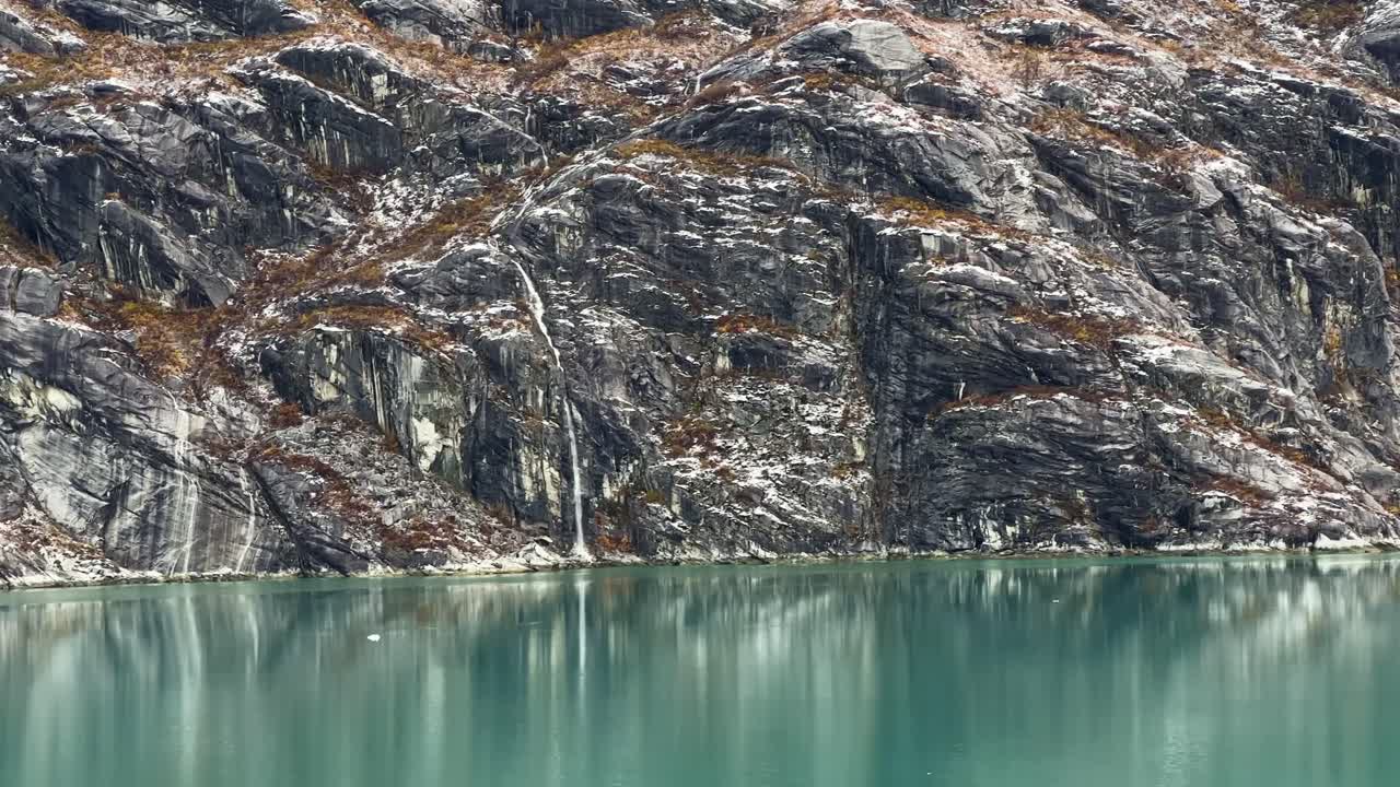 Handheld telephoto dolly shot of waterfalls running down frozen rocks near Topeka Glacier in Glacier Bay, Alaska. 4K