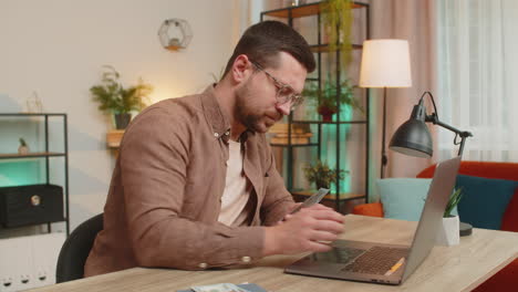 rich happy caucasian man counting money cash using laptop calculate domestic bills at home table