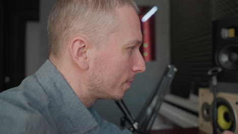 close-up of a man in a blue shirt focused and busy in a studio room with a grey background. the man appears to be engaged in a task, likely related to audio or video production