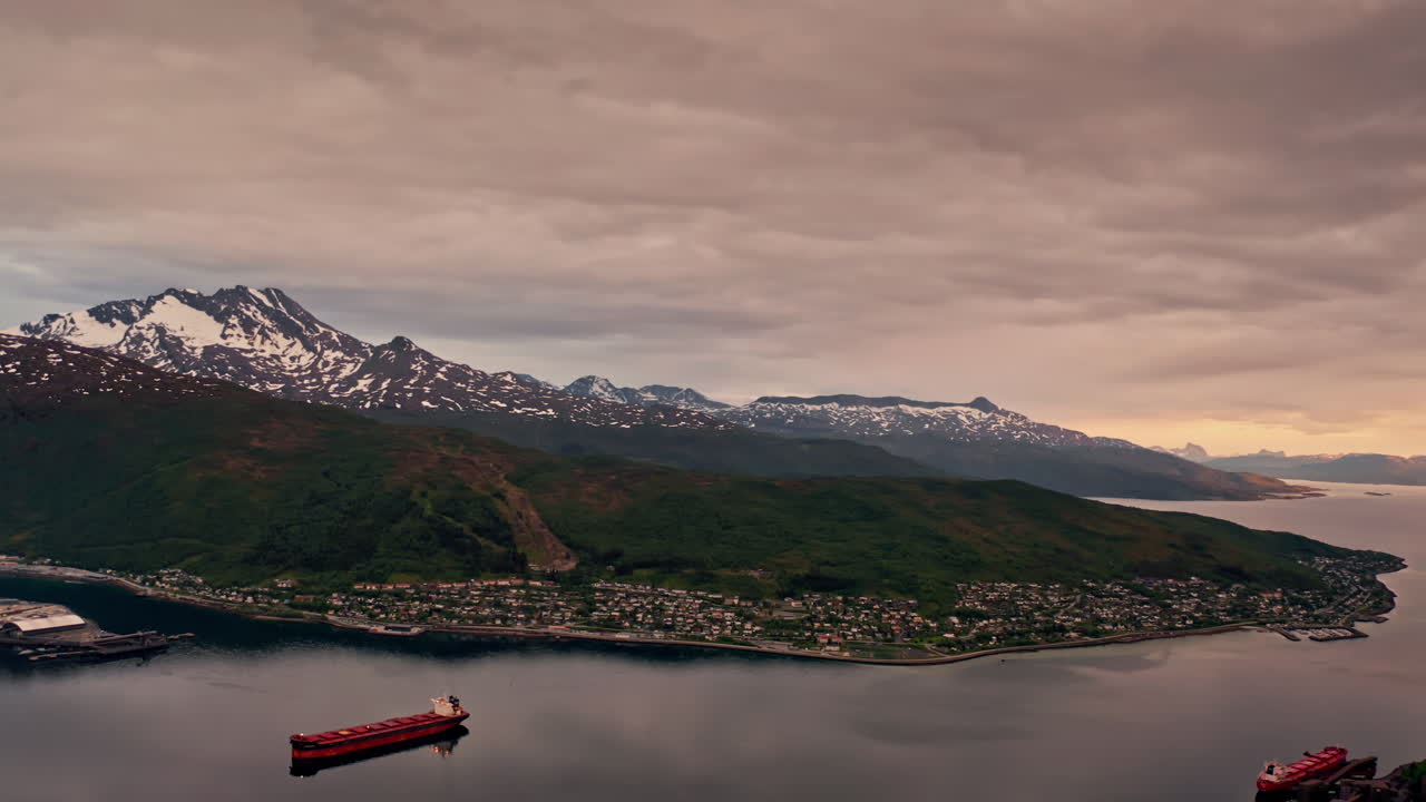Aerial drone shot over the city of Narvik in Norway at sunset. High view of the nordic city located at the coastline. View of the sea and the mountains in the distance.