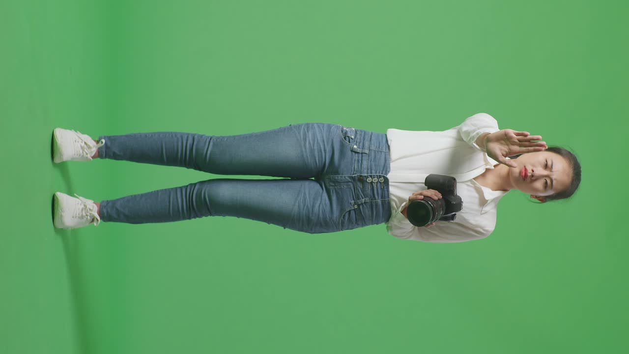Full Body Of Asian Photographer Using A Camera Taking Pictures And Making Stop Hand Sign While Standing On Green Screen Background In The Studio
